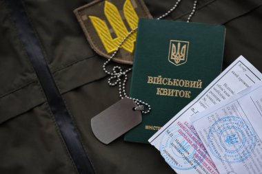 Military token or army ID ticket with mobilization notice lies on green ukrainian military uniform indoors close up clipart