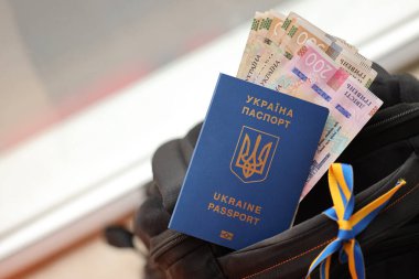 Ukrayna biyometrik pasaportu ve UAH para faturaları turistik sırt çantasına yakın.