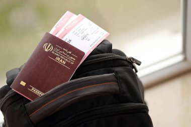 Red Islamic Republic of Iran passport with airline tickets on touristic backpack close up. Tourism and travel concept clipart