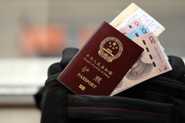 Çin Halk Cumhuriyeti 'nin kırmızı pasaportu ve sırt çantasında uçak biletleri olan Çin Yuan' ı. PRC pasaportu