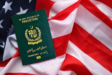 Pakistan 'ın yeşil İslam Cumhuriyeti pasaportu ABD bayrağının arka planında, yakın plan. Turizm ve diplomasi kavramı