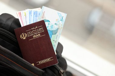 Red Islamic Republic of Iran passport with money and airline tickets on touristic backpack close up. Tourism and travel concept clipart
