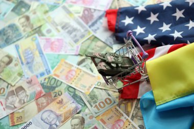 Amerikan bayrağında oyuncak tank ve farklı para birimlerinde Ukrayna bayrağı. ABD ile Ukrayna arasındaki savaş finansmanı ve askeri desteğin arka planı