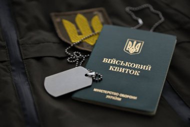 Military token or army ID ticket lies on green ukrainian military uniform indoors close up clipart
