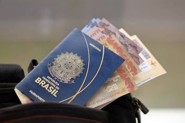Blue Brazilian passport with money and airline tickets on touristic backpack close up. Tourism and travel concept clipart