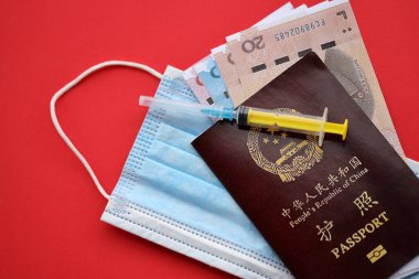 Çin Halk Cumhuriyeti 'nin kırmızı pasaportu ve şırıngalı ve maskeli Çin Yuan paraları. Parlak arkaplanda PRC Çin pasaportu