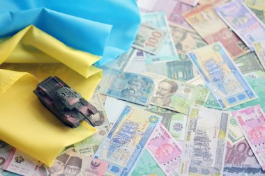 Ukrayna bayrağında farklı para birimlerinde oyuncak tankı. Ukrayna 'daki savaş finansmanı ve askeri destek fiyatlarının geçmişi