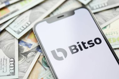KYIV, UKRAINE - 15 Mart 2024 Bitso logosu iPhone ekranında yüzlerce dolarlık banknotlarla. Kripto döviz portalı