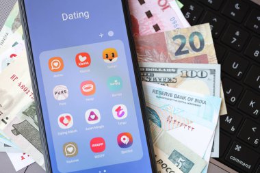 KYIV, UKRAINE - FEBRUARY 28, 2024 Dating apps icons on smartphone display on MacBook keyboard and money bills of different currencies clipart