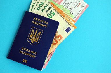 Ukrayna biyometrik pasaportu ve Avrupa Avro para faturaları ve mavi arka planda uçak biletleri.