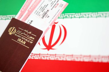 Red Islamic Republic of Iran passport with airline tickets on Iranian flag background close up. Tourism and travel concept clipart