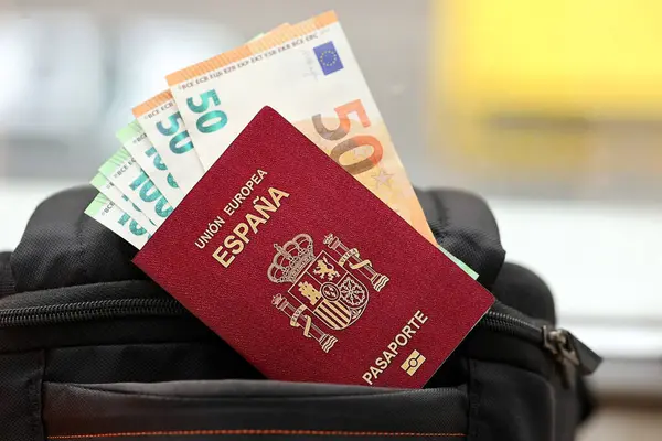 Red Spanish passport of European Union with money and airline tickets on touristic backpack close up. Tourism and travel concept