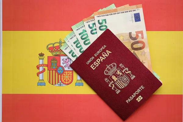 Red Spanish passport of European Union and money on flag background close up. Tourism and citizenship concept