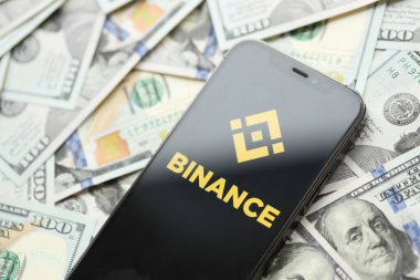 KYIV, UKRAINE - 15 Mart 2024 Binance logosu iPhone ekranında yüzlerce dolarlık banknotlarla. Kripto döviz portalı
