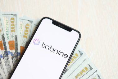 KYIV, UKRAINE - 17 Mart 2024 Tabnine logosu iPhone ekranında yüzlerce dolarlık banknotlarla. Yapay Zeka Motoru