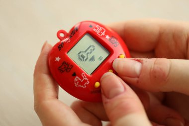 KYIV, UKRAINE - 9 Mart 2024 Retro evcil hayvan zinciri oyunu tamagotchi kırmızı plastik çantada kadınların elinde yakın plan