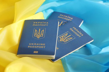 Three Ukrainian biometrical passports on folded waving flag of Ukraine country close up clipart