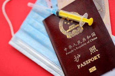 Çin Halk Cumhuriyeti 'nin kırmızı pasaportu ve şırıngalı ve maskeli Çin Yuan paraları. Parlak arkaplanda PRC Çin pasaportu