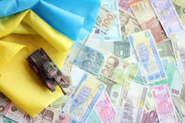 Ukrayna bayrağında farklı para birimlerinde oyuncak tankı. Ukrayna 'daki savaş finansmanı ve askeri destek fiyatlarının geçmişi