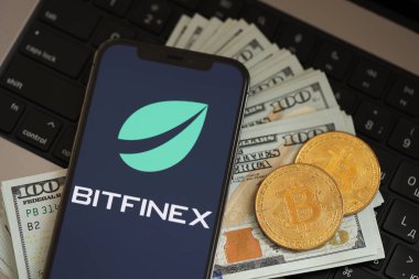 KYIV, UKRAINE - 15 Mart 2024 Btfinex logosu iPhone ekranında dolar ve bitcoin ile MacBook. Kripto döviz portalı