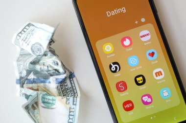 KYIV, UKRAINE - FEBRUARY 28, 2024 Dating apps icons on smartphone display on MacBook keyboard and crumpled US dollar bill clipart