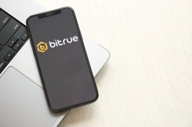 KYIV, UKRAINE - 15 Mart 2024 Bitrue logosu MacBook panelinde iPhone ekranında. iPhone ekranında şifreli döviz portalı logosu ve MacBook 'ta dolar ve bitcoin var. Kripto para birimi