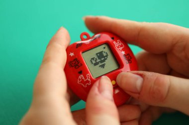 KYIV, UKRAINE - 9 Mart 2024 Retro evcil hayvan zinciri oyunu tamagotchi kırmızı plastik çantada kadınların elinde yakın plan