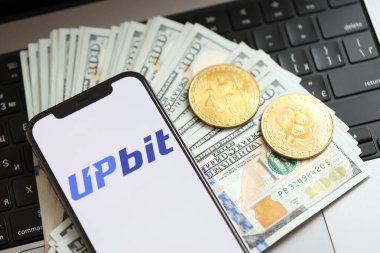 KYIV, UKRAINE - 15 Mart 2024 Upbit logosu iPhone ekranında dolar ve bitcoin ile MacBook 'ta. Kripto döviz portalı