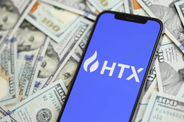 KYIV, UKRAINE - 15 Mart 2024 HTX logosu iPhone ekranında yüzlerce dolarlık banknotlarla. Kripto döviz portalı
