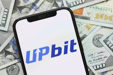 KYIV, UKRAINE - 15 Mart 2024 Upbit logosu iPhone ekranında yüzlerce dolarlık banknotlarla. Kripto döviz portalı