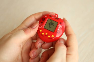KYIV, UKRAINE - 9 Mart 2024 Retro evcil hayvan zinciri oyunu tamagotchi kırmızı plastik çantada kadınların elinde yakın plan