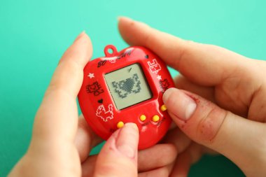 KYIV, UKRAINE - 9 Mart 2024 Retro evcil hayvan zinciri oyunu tamagotchi kırmızı plastik çantada kadınların elinde yakın plan