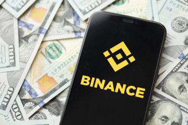 KYIV, UKRAINE - 15 Mart 2024 Binance logosu iPhone ekranında yüzlerce dolarlık banknotlarla. Kripto döviz portalı