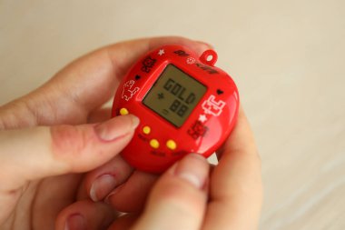 KYIV, UKRAINE - 9 Mart 2024 Retro evcil hayvan zinciri oyunu tamagotchi kırmızı plastik çantada kadınların elinde yakın plan