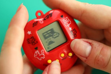 KYIV, UKRAINE - 9 Mart 2024 Retro evcil hayvan zinciri oyunu tamagotchi kırmızı plastik çantada kadınların elinde yakın plan