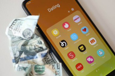 KYIV, UKRAINE - 28 Şubat 2024 MacBook klavyesinde akıllı telefon ekran simgeleri ve buruşmuş Amerikan doları