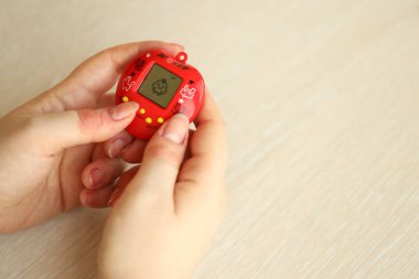 KYIV, UKRAINE - 9 Mart 2024 Retro evcil hayvan zinciri oyunu tamagotchi kırmızı plastik çantada kadınların elinde yakın plan