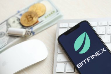 KYIV, UKRAINE - 15 Mart 2024 Btfinex logosu iPhone ekranında para ve bitcoin ile birlikte beyaz klavyede. Kripto döviz portalı