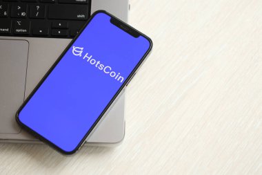 KYIV, UKRAINE - 15 Mart 2024 Hotscoin logosu MacBook panelinde iPhone ekranında. iPhone ekranındaki şifreli döviz portalı logosu ve MacBook 'ta dolar ve bitcoin' ler.