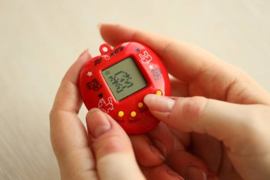 KYIV, UKRAINE - 9 Mart 2024 Retro evcil hayvan zinciri oyunu tamagotchi kırmızı plastik çantada kadınların elinde yakın plan