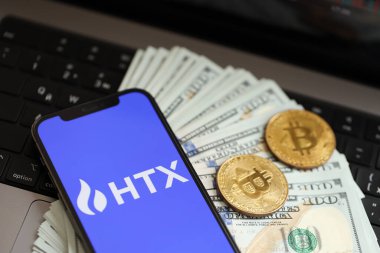 KYIV, UKRAINE - 15 Mart 2024 HTX logosu iPhone ekranında dolar ve bitcoin ile MacBook. Kripto döviz portalı