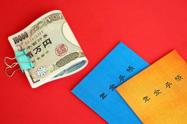 Japon emeklilik sigortası broşürleri yen para faturalarıyla dolu masada. Japon emekliler için mavi ve turuncu kitaplar kapanıyor.