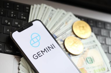 KYIV, UKRAINE - 15 Mart 2024 Gemini logosu iPhone ekranında dolar ve bitcoin ile MacBook 'ta. Kripto döviz portalı