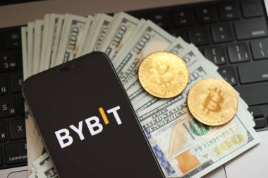 KYIV, UKRAINE - 15 Mart 2024 Bybit logosu iPhone ekranında dolar ve bitcoin ile MacBook üzerinde. Kripto döviz portalı