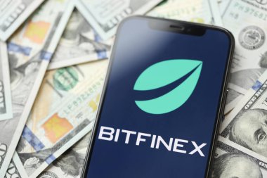 KYIV, UKRAINE - 15 Mart 2024 Btfinex logosu iPhone ekranında yüzlerce dolarlık banknotlarla. Kripto döviz portalı