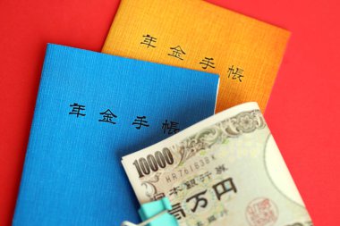 Japon emeklilik sigortası broşürleri yen para faturalarıyla dolu masada. Japon emekliler için mavi ve turuncu kitaplar kapanıyor.