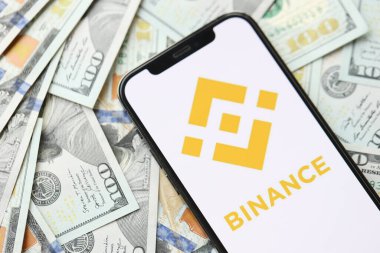 KYIV, UKRAINE - 15 Mart 2024 Binance logosu iPhone ekranında yüzlerce dolarlık banknotlarla. Kripto döviz portalı