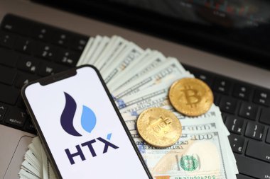 KYIV, UKRAINE - 15 Mart 2024 HTX logosu iPhone ekranında dolar ve bitcoin ile MacBook. Kripto döviz portalı