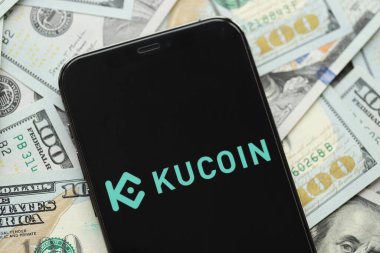 KYIV, UKRAINE - 15 Mart 2024 Kucoin logosu iPhone ekranında yüzlerce dolarlık banknotlarla. Kripto döviz portalı