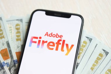 KYIV, UKRAINE - 17 Mart 2024 Adobe Firefly logosu iPhone ekranında yüzlerce dolarlık banknotlarla. Yapay Zeka Motoru